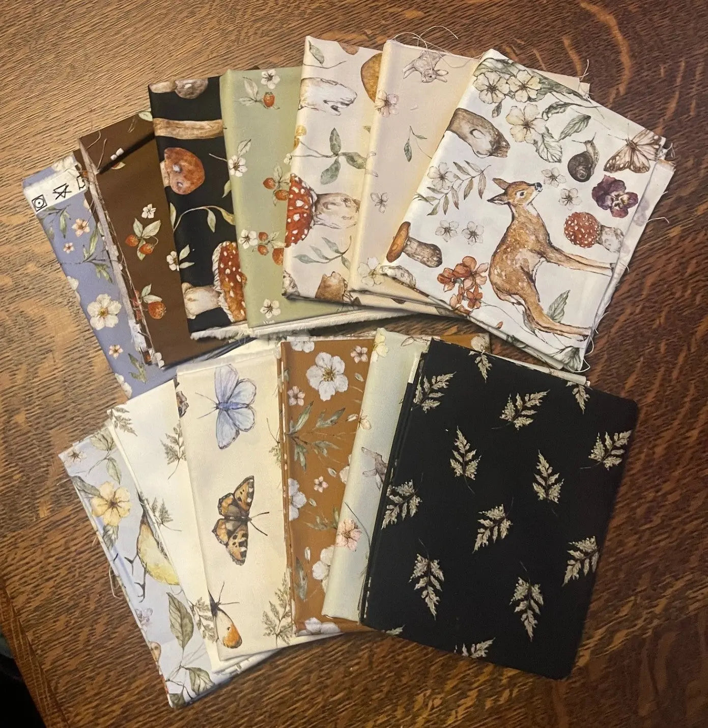 Collection of fabric swatches with various patterns on a wooden surface. from heavenly hedgerow fat quarter bundle.