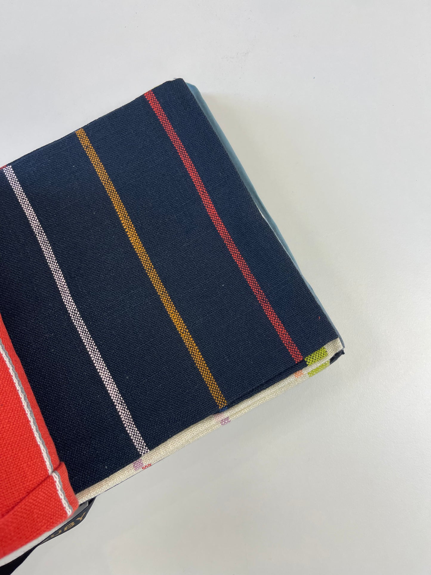 A close-up of a folded navy blue fabric item with vertical stripes in red, mustard yellow, white, and light blue, shown on a plain white background.