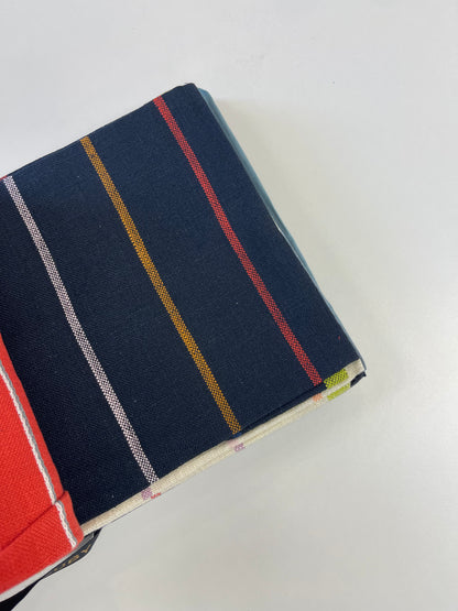 A close-up of a folded navy blue fabric item with vertical stripes in red, mustard yellow, white, and light blue, shown on a plain white background.