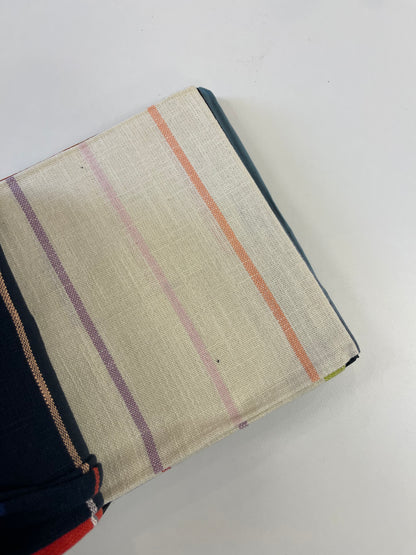 A close-up of a woven fabric cover or pouch with a cream base and vertical stripes in orange, purple, and pink, shown on a plain white background.