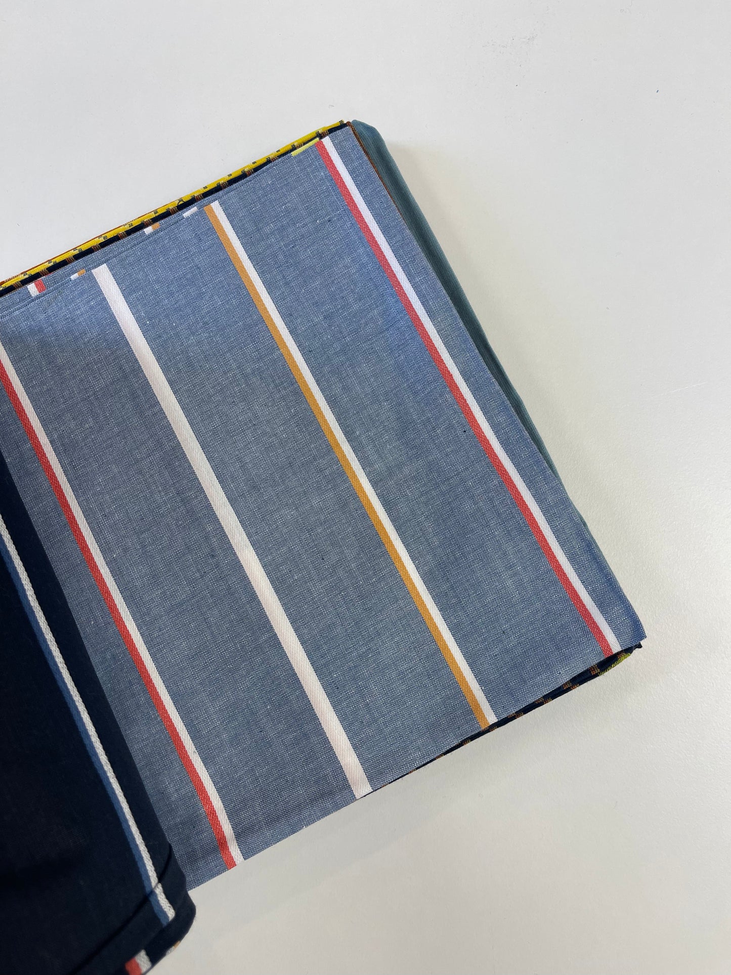 A folded piece of blue-gray striped fabric with vertical white, yellow, and red stripes, shown on a plain white background.