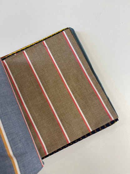 A close-up of a striped fabric or textile sample laid on a white background, showing a brown base with vertical red, white, and thin yellow stripes, plus a blue-gray section along the left edge.