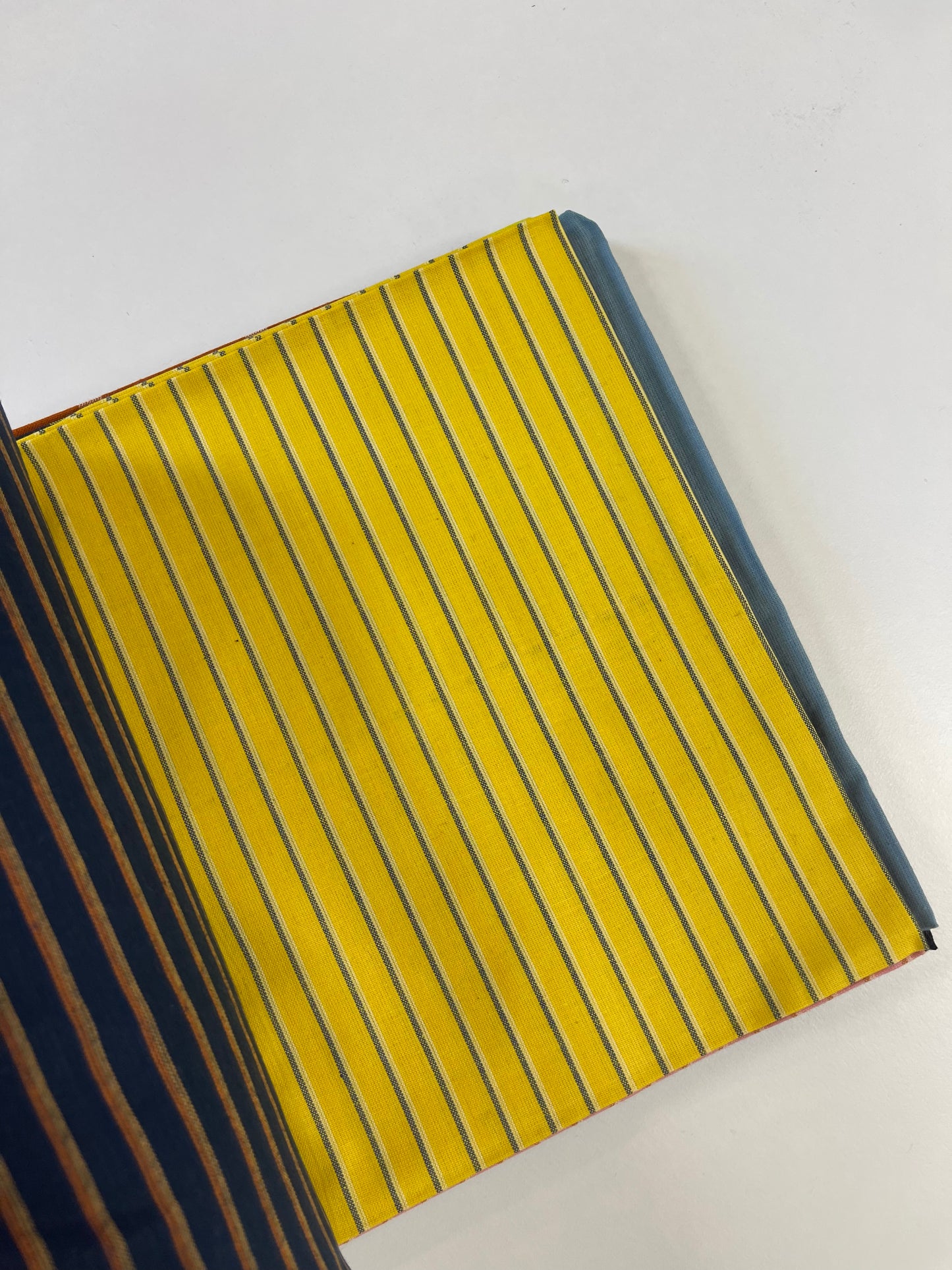 A close-up of a striped fabric or leather material sample with a bright yellow base and thin dark blue vertical stripes, shown on a plain white background.
