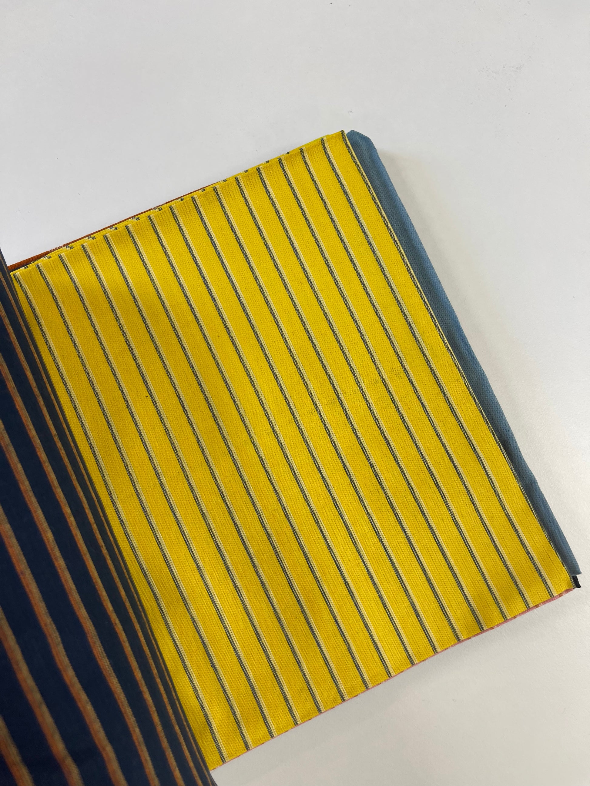 A close-up of a striped fabric or leather material sample with a bright yellow base and thin dark blue vertical stripes, shown on a plain white background.