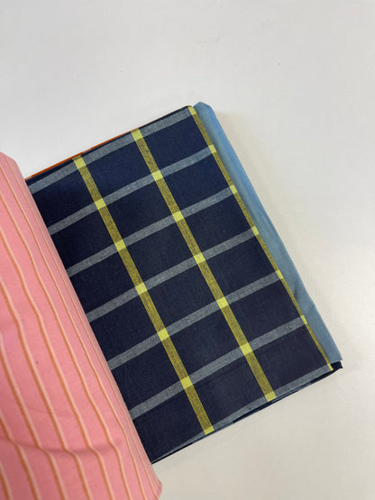 A close-up of a navy blue fabric item, likely a notebook cover or book sleeve, featuring a yellow and gray plaid pattern, with a pink striped fabric partially visible on the left.