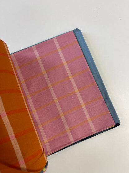A folded piece of pink plaid fabric with orange and white stripes, layered over a blue fabric, with a folded orange striped fabric visible on the left, set against a plain white background.