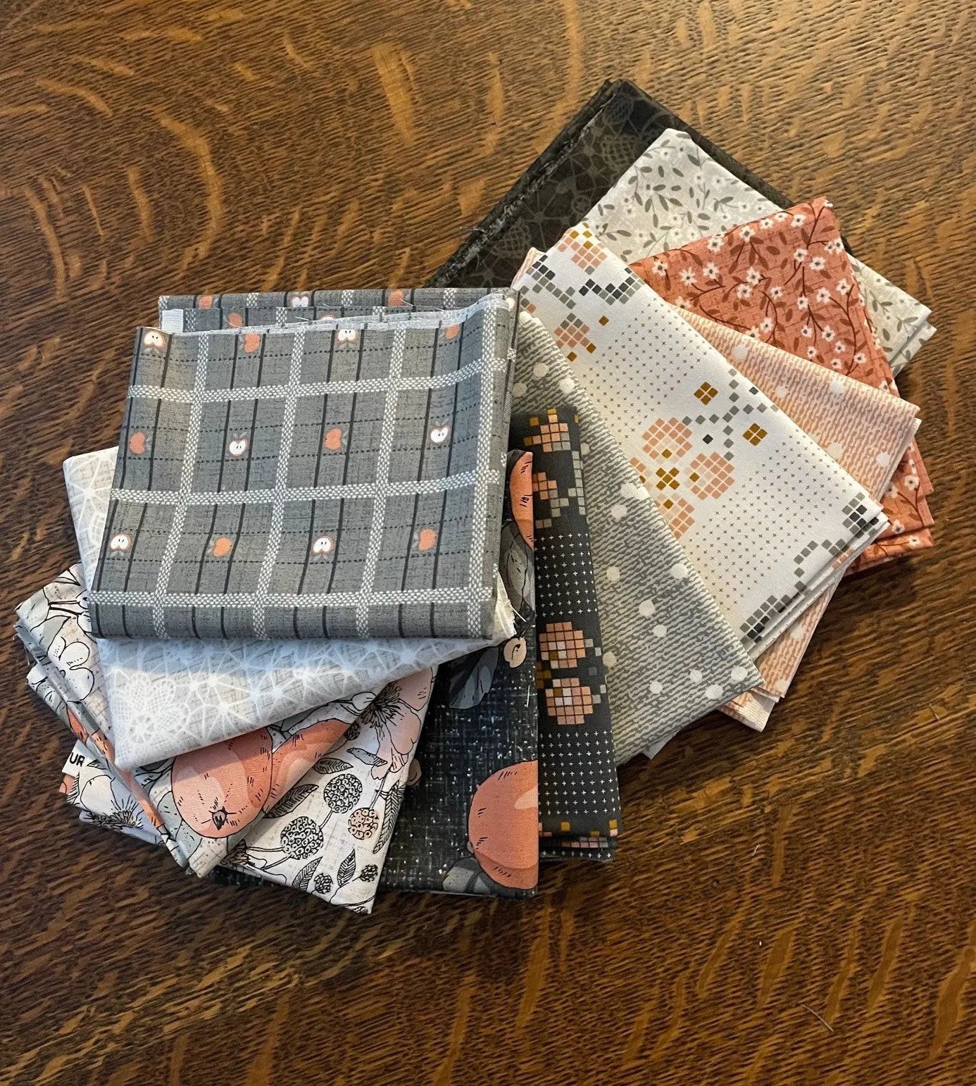 A pile of assorted 12 fat quarter pieces from the line Klara from FIGO Fabrics in various patterns and colors, arranged on a wooden surface. 