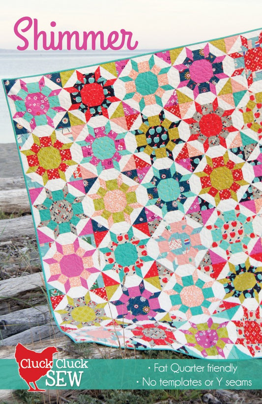 Colorful quilt with geometric pattern on a wooden surface, featuring the brand 'Cluck Cluck Sew'.