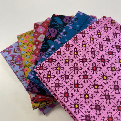 A stack of folded patterned fabric pieces fanned out on a white surface, showing multiple colorful designs including pink, blue, yellow, and purple geometric and floral motifs.