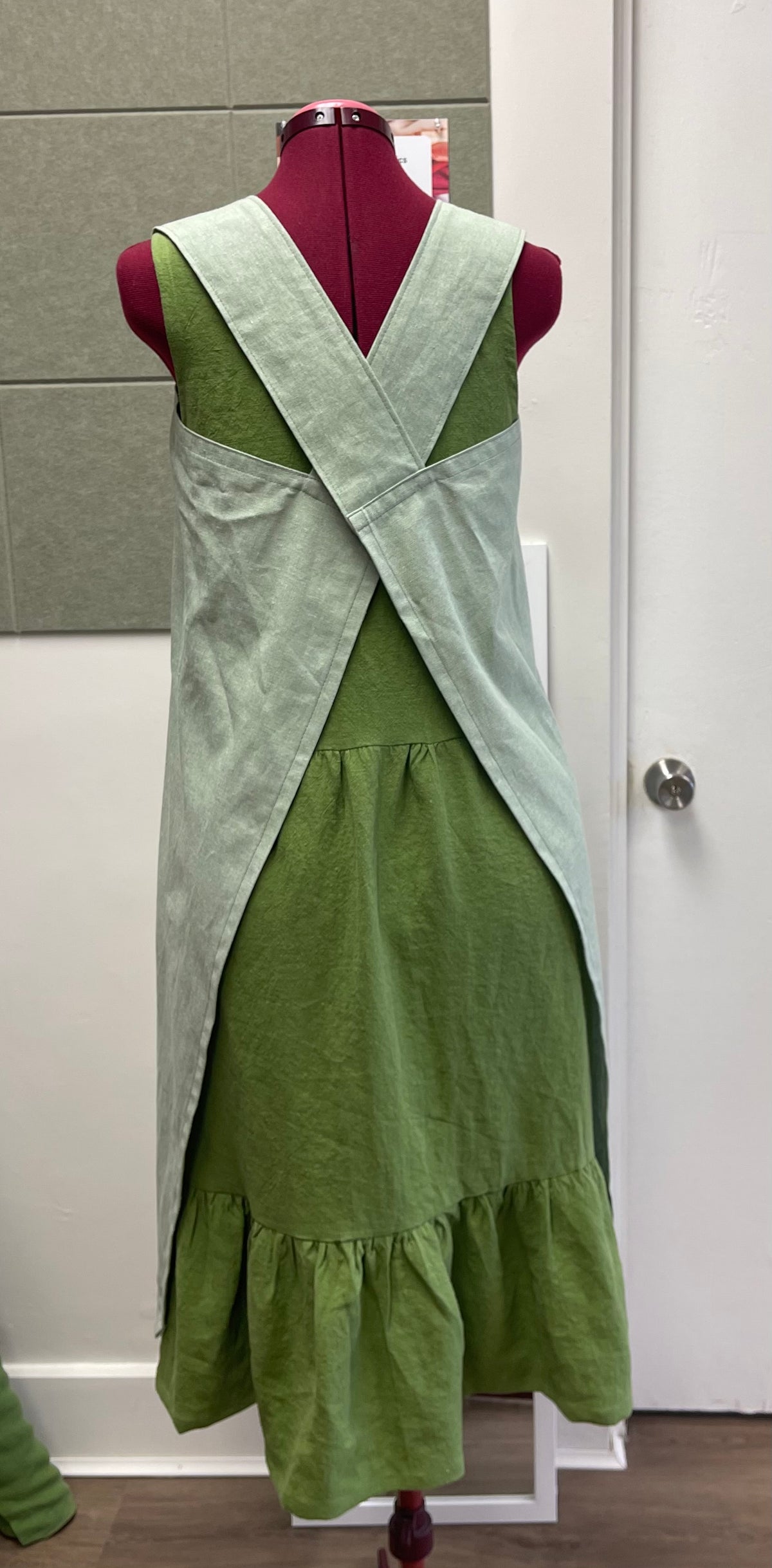 a cross back apron in cotton linen blend displayed on a sewing dummy for sewing lesson and workshop.