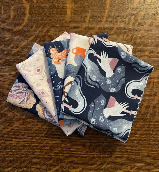 A stack of five different patterned fat quarters of cotton fabric, displayed on a wooden surface. Science based theme