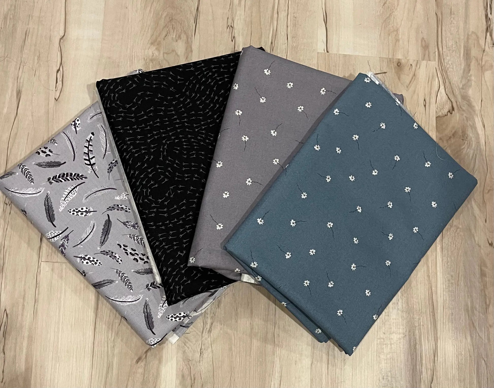A selection of fabric remnants bundled together, featuring a variety of patterns including floral, geometric, and dots, primarily in black, blue, and gray colors.