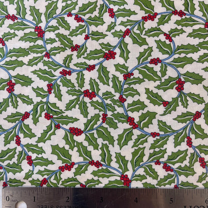 A close-up of patterned fabric with a repeating holly design featuring green leaves, red berries, and blue stems on an off-white background from Liberty of London Fabrics for quilting and crafting.