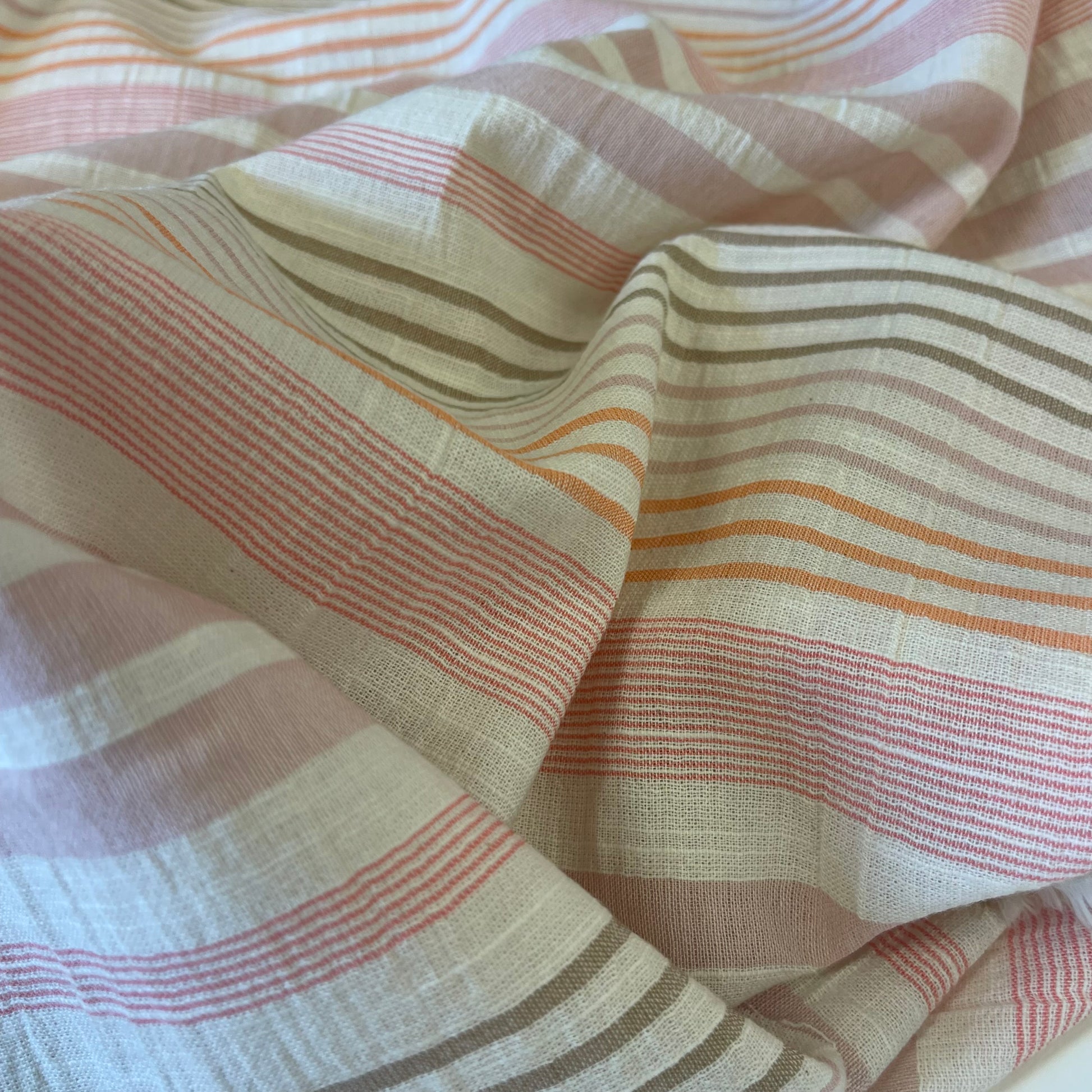 Striped cotton viscose lightweight fabric with pink, orange, and beige colors for sewing garments. 