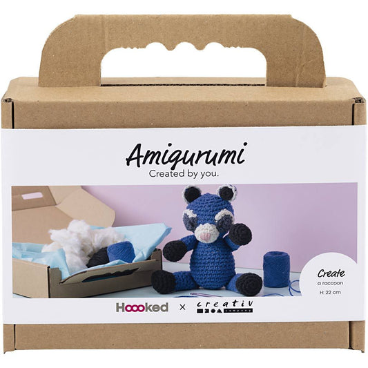 Amigurumi crochet kit packaging with a blue raccoon toy and crafting materials on a white background.