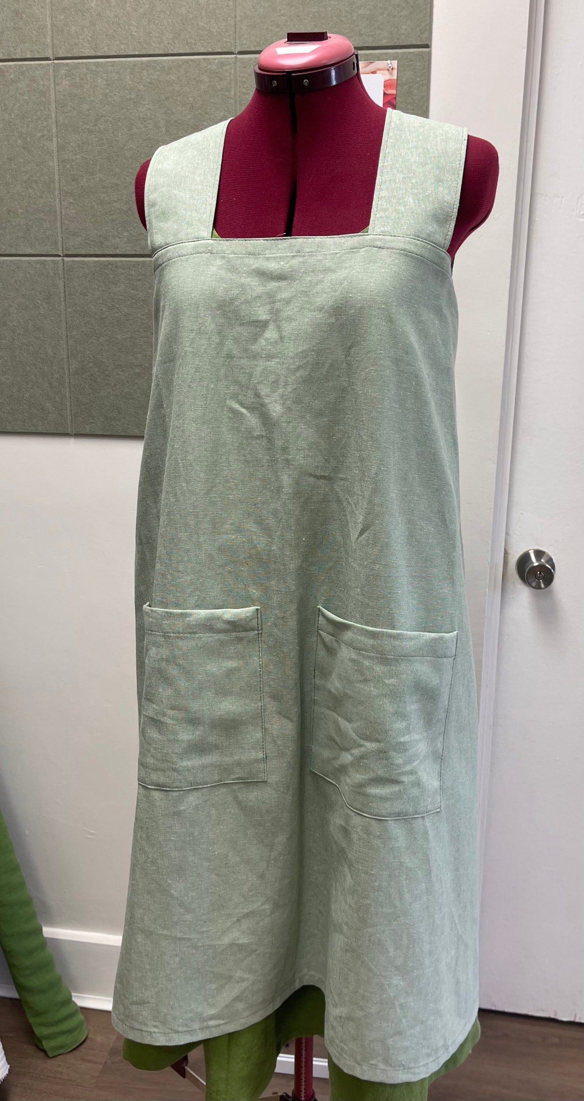 a cross back apron in cotton linen blend displayed on a sewing dummy for sewing lesson and workshop.