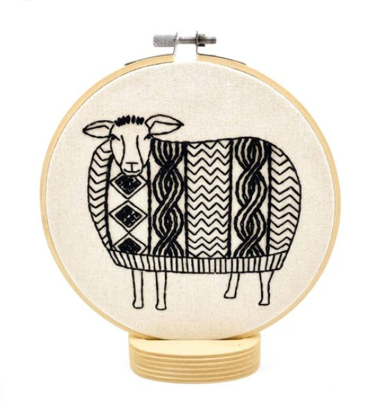 Embroidery hoop with a black and white patterned sheep design on beige fabric.