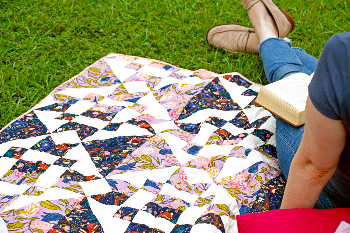 Person sitting on a colorful quilt reading a book outdoors.