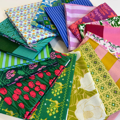 A collection of colorful patterned fat quarter fabric squares arranged in a circular stack on a plain white background. Form Anna Maria Textiles for quilting and sewing. 