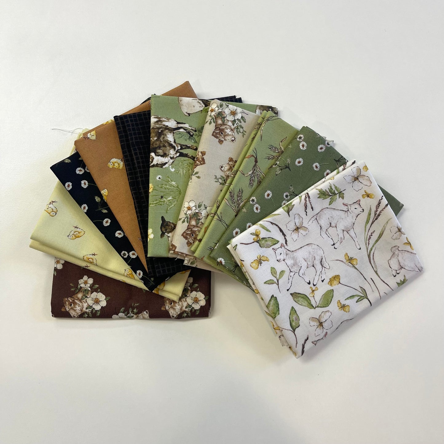 A fan arrangement of multiple fabric squares with different prints, including floral, animal, and botanical designs in muted green, beige, brown, black, and cream tones, photographed on a plain white background.