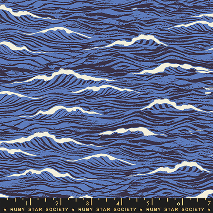 A close-up of a fabric pattern featuring stylized blue ocean waves with white crests and dark navy linework, with a Ruby Star Society ruler visible along the bottom edge.