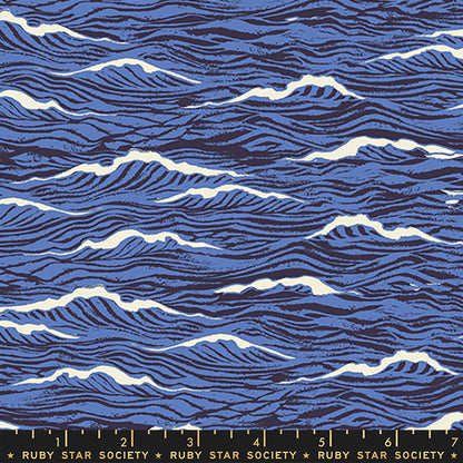 A close-up of a fabric pattern featuring stylized blue ocean waves with white crests and dark navy linework, with a Ruby Star Society ruler visible along the bottom edge.