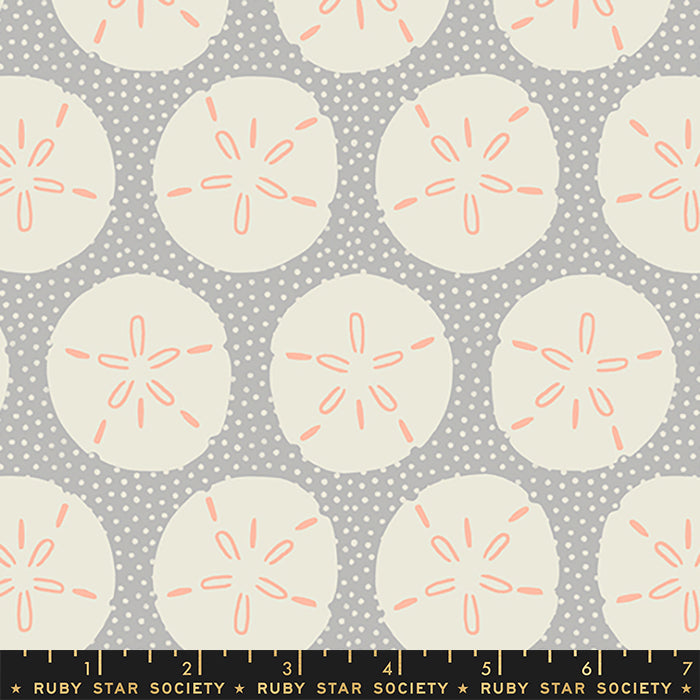 A repeating fabric pattern featuring cream sand dollars with coral-orange centers on a gray polka-dot background, with a Ruby Star Society ruler along the bottom edge.