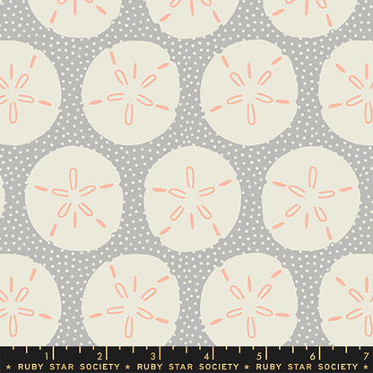 A repeating fabric pattern featuring cream sand dollars with coral-orange centers on a gray polka-dot background, with a Ruby Star Society ruler along the bottom edge.