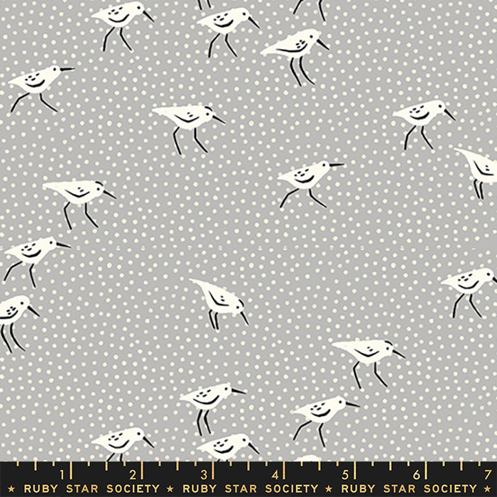 Fabric with a repeating pattern of white sandpipers with black legs and beaks on a light gray background with small white polka dots. A black ruler at the bottom shows measurements and the brand name Ruby Star Society.