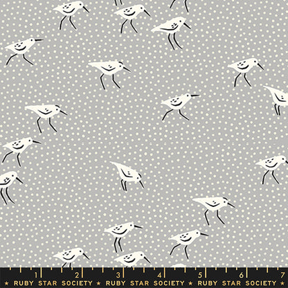 Fabric with a repeating pattern of white sandpipers with black legs and beaks on a light gray background with small white polka dots. A black ruler at the bottom shows measurements and the brand name Ruby Star Society.