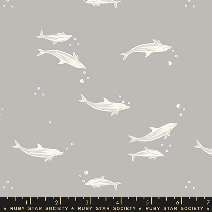 Gray fabric with a repeating pattern of white dolphins swimming underwater, accented with small white bubbles. A black ruler at the bottom shows the scale of the pattern with 'Ruby Star Society' branding.