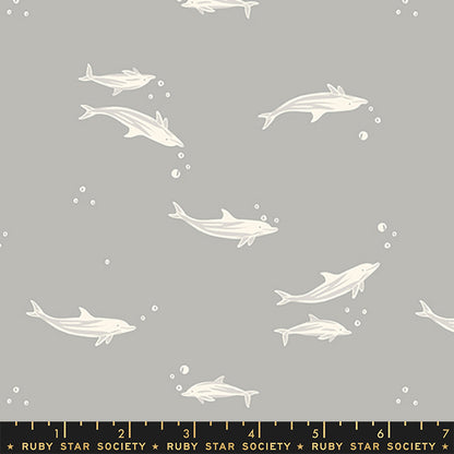Gray fabric with a repeating pattern of white dolphins swimming underwater, accented with small white bubbles. A black ruler at the bottom shows the scale of the pattern with 'Ruby Star Society' branding.