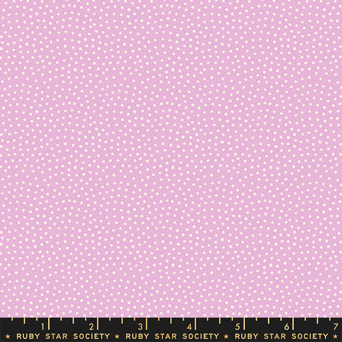 A close-up of a pink fabric with a repeating pattern of small white dots, with a black measuring ruler along the bottom edge labeled Ruby Star Society.