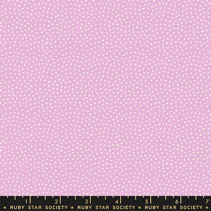 A close-up of a pink fabric with a repeating pattern of small white dots, with a black measuring ruler along the bottom edge labeled Ruby Star Society.