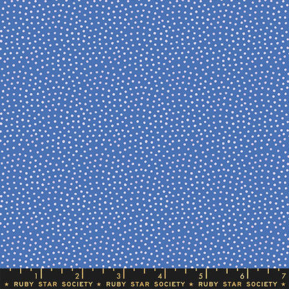 A close-up of blue fabric with a repeating pattern of small white dots, with a black ruler along the bottom edge labeled Ruby Star Society.