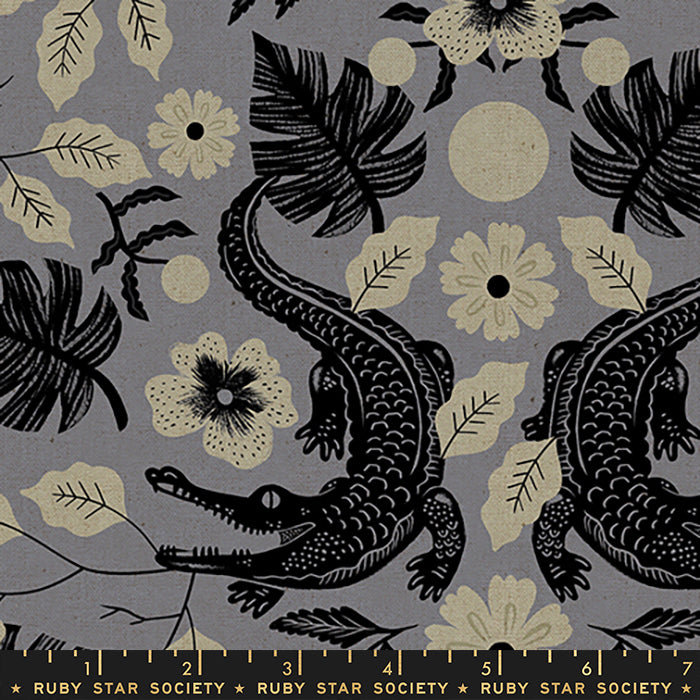 A close-up of a fabric pattern featuring black alligators, tropical leaves, and cream flowers on a muted gray background, with a Ruby Star Society ruler printed along the bottom edge.