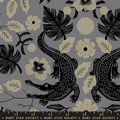 A close-up of a fabric pattern featuring black alligators, tropical leaves, and cream flowers on a muted gray background, with a Ruby Star Society ruler printed along the bottom edge.