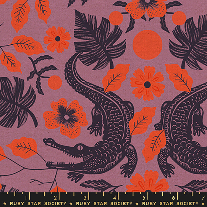 A close-up of a patterned fabric featuring black alligators and orange tropical leaves and flowers on a muted mauve-purple background, with a Ruby Star Society ruler along the bottom edge.