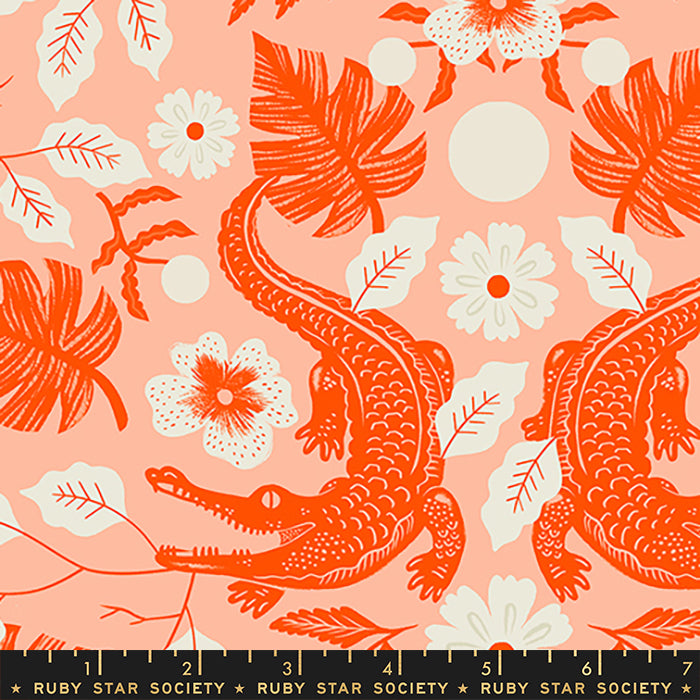 Fabric with a repeating tropical print featuring orange alligators, white flowers, and orange leaves on a peach-pink background, with a black ruler strip at the bottom showing the Ruby Star Society branding and measurements.