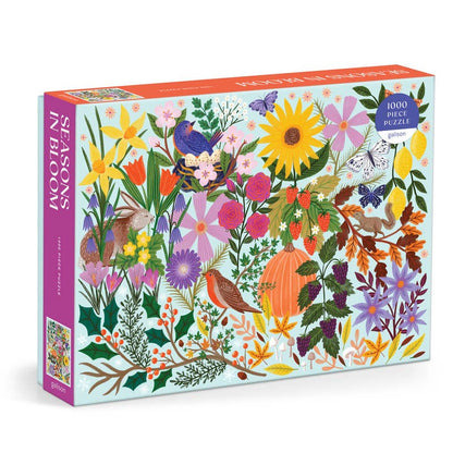 A 1000-piece jigsaw puzzle box titled 'Seasons in Bloom' featuring a colorful, dense illustration of spring flowers, birds, butterflies, and autumn leaves on a light blue background.