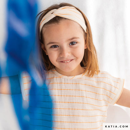 Young girl wearing a striped headband and shirt, smiling at the camera.
