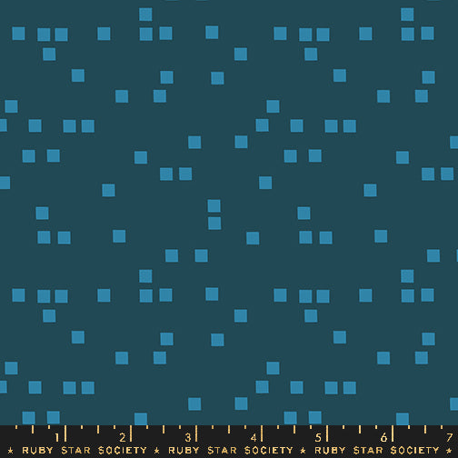 A close-up of a fabric pattern featuring small light blue squares scattered across a dark teal background, with a measuring ruler along the bottom edge labeled Ruby Star Society.