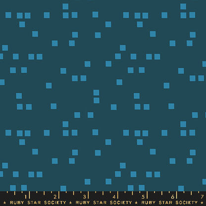 A close-up of a fabric pattern featuring small light blue squares scattered across a dark teal background, with a measuring ruler along the bottom edge labeled Ruby Star Society.