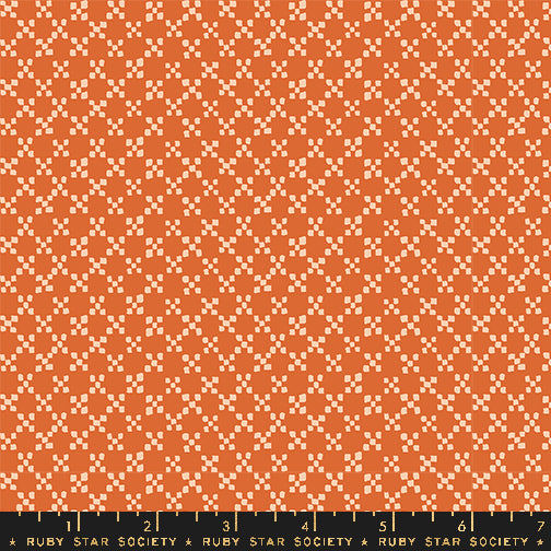 A close-up of a repeating geometric fabric pattern in orange and cream, with a black ruler along the bottom edge labeled Ruby Star Society.