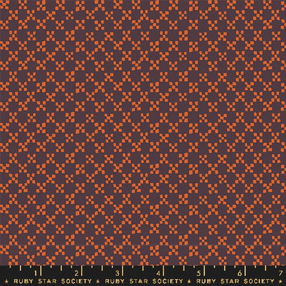 A close-up fabric pattern swatch showing a repeating geometric design in rust orange and dark plum purple, with a Ruby Star Society ruler along the bottom edge for scale.