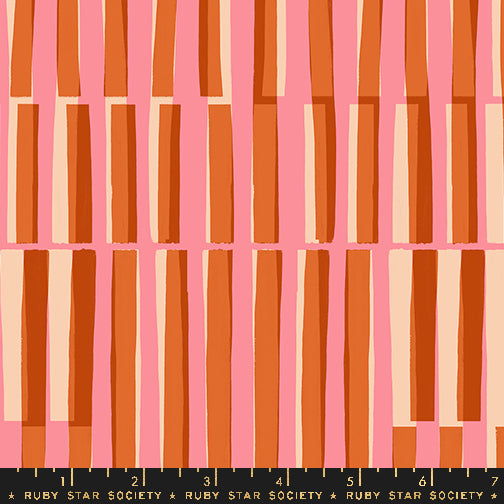 Fabric with a repeating geometric pattern of vertical rectangular bars in orange, rust, peach, and cream on a pink background, with a black ruler strip labeled RUBY STAR SOCIETY along the bottom edge.