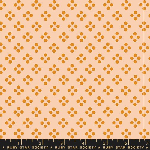A repeating fabric pattern featuring small orange-brown floral clusters on a warm peach background, with a black Ruby Star Society ruler along the bottom edge.