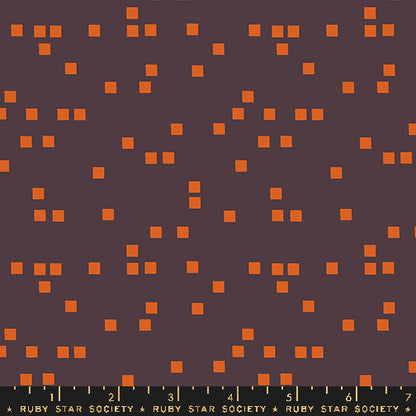 A close-up fabric or material swatch showing a dark brown background with scattered small orange square motifs and a black ruler strip along the bottom labeled Ruby Star Society.