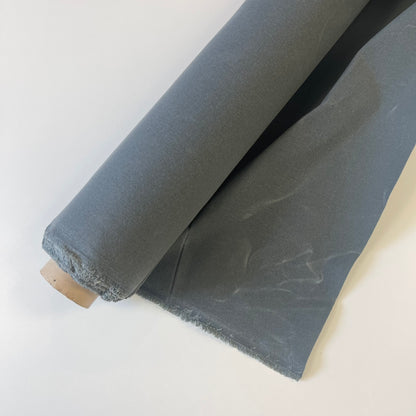 A roll of dark medium waxed canvas fabric with a frayed edge, partially unrolled on a plain white background.