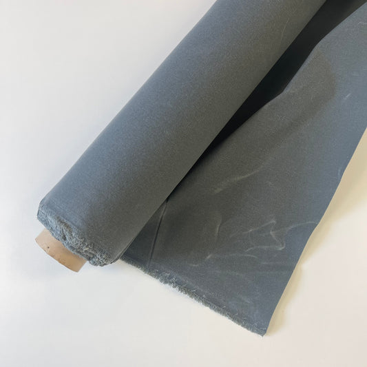 A roll of dark medium waxed canvas fabric with a frayed edge, partially unrolled on a plain white background.